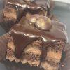 Detailed view of individual chocolate cakes with layers of cake and filling, topped with a glossy chocolate ganache and decorative chocolate pieces, on a dark gray plate.