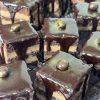Close-up of square amandine cakes with chocolate glaze, layered filling, and a gold candy on top.